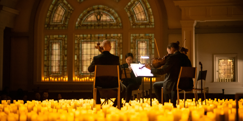 A string quartet performs on the Great Hall stage surrounded by lit candles.