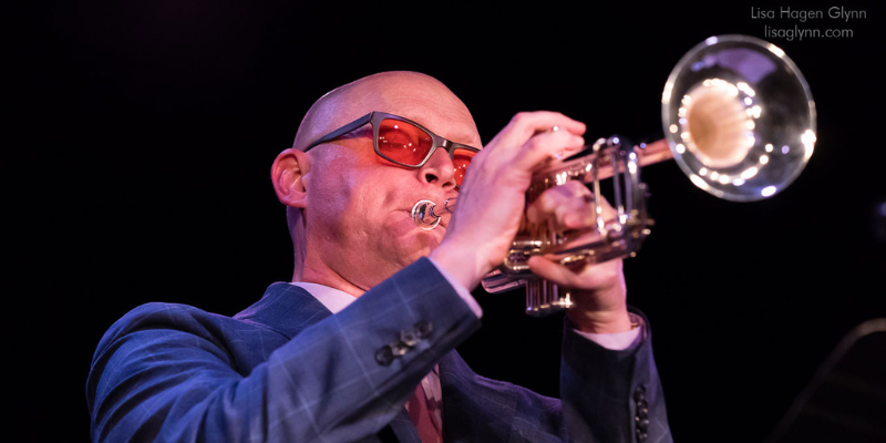 Close-up shot of Thomas Marriott (with sunglasses and navy suit) playing the trumpet