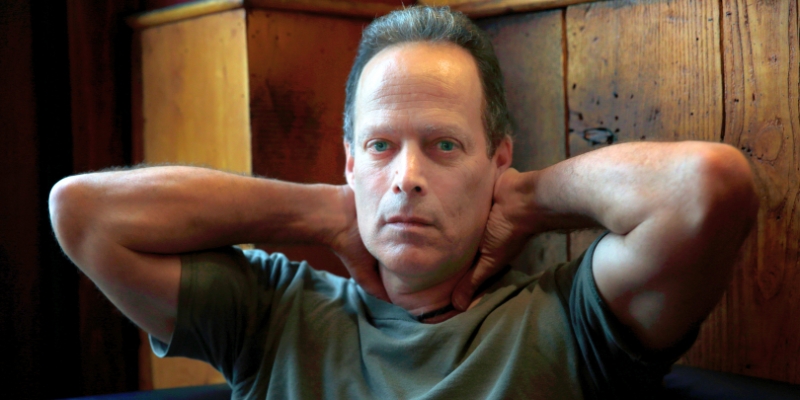 Headshot of Sebastian Junger (with fair skin and short grey hair). His hands are placed behind his head.