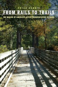 Book cover: A wooden bridge stands in a green forest, covered in shadows. Title at the top says "From Rails to Trails: The Making of America's Active Transportation Network"
