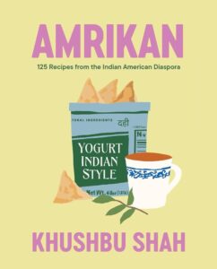 Book cover: The title "AMRIKAN" is displayed at the top in large, bold letters. Below the title, the subtitle "Recipes from the Indian American Diaspora" is shown in smaller text. The background is a light yellow, and in the center of the cover, there are illustrations of a yogurt container labeled “yogurt indian style” and a teacup