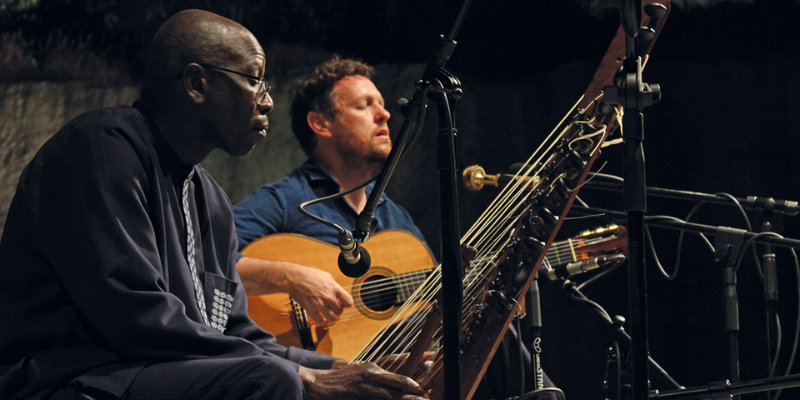 Side shot of Ballake Sissoko playing the kora (an African stringed instrument) and Derek Gripper playing the guitar.