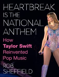 Book cover of 'Heartbreak Is The National Anthem: How Taylor Swift Reinvented Pop Music' by Rob Sheffield featuring Taylor Swift in a sparkling bodysuit holding a microphone, with bold white and pink text on a black background.