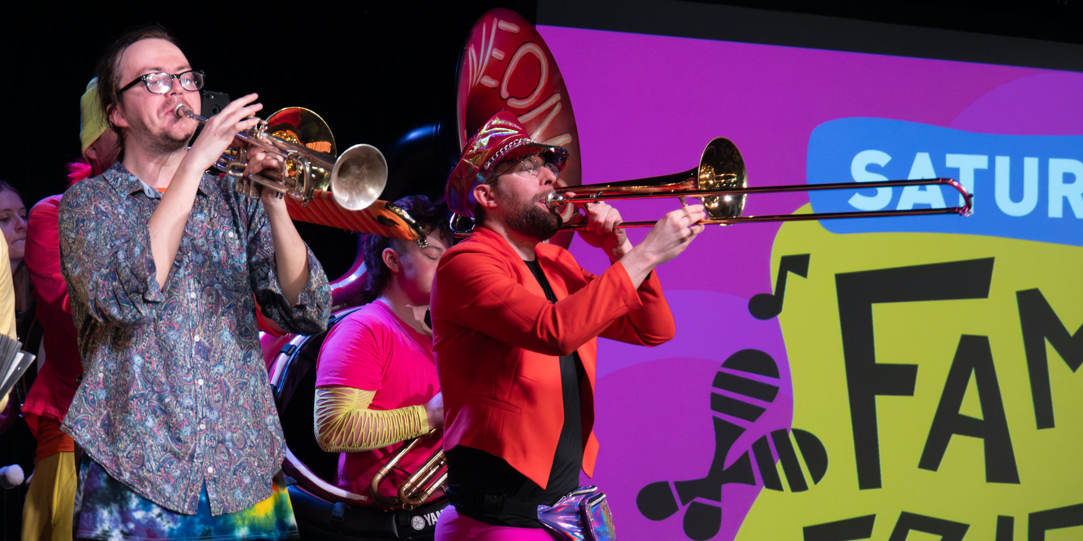 Musicians in brightly colored clothing play the trumpet and trombone