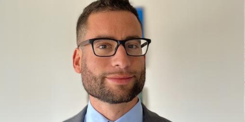 Headshot of Jake Grumbach (with light skin, cropped brown hair, eyeglasses, and beard)