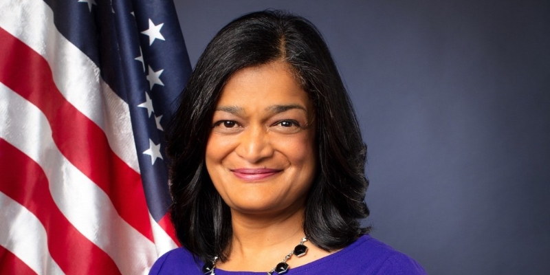 Headshot of Pramila Jayapal (with tan skin and black bob haircut) standing in front of the USA flag.