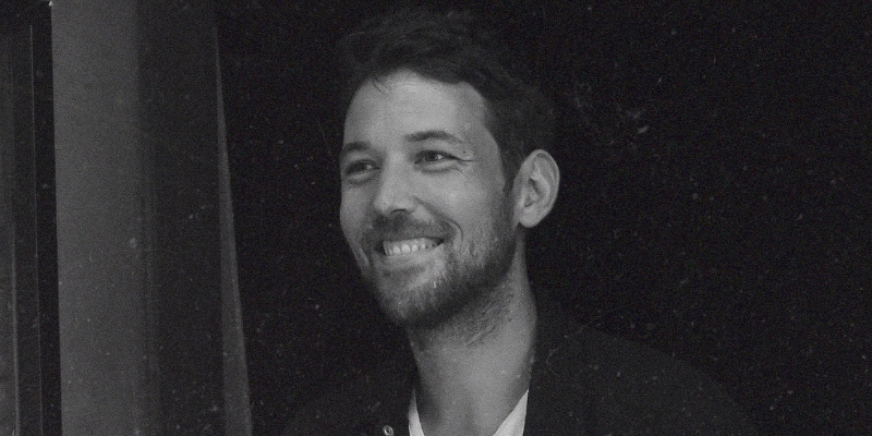 Black & white headshot of Robin Pecknold (with light skin, short dark hair, and beard)