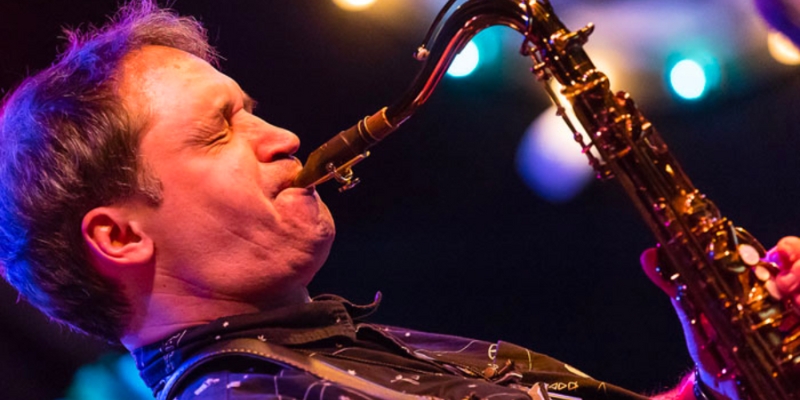 Close up shot of a person with fair skin and short hair playing the saxophone.