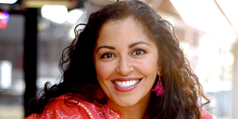 Headshot of Aimee Nezhukumatathil (with tan skin, long wavy black hair, and pink feather earrings)