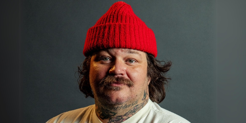 Headshot of Matty Matheson (with brown hair, mustache, red beanie, and upper body tattoos)