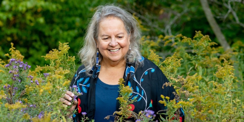 Headshot of Robin Wall Kimmerer (with light skin, shoulder-length grey hair, and blue floral blouse)