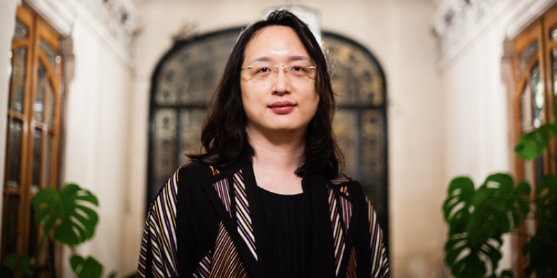 Headshot of Audrey Tang (with fair skin, shoulder-length black hair, eyeglasses, and striped black jacket)