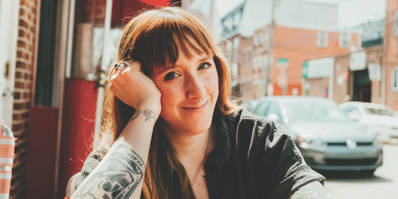 Headshot of Kelsey McKinnon (with fair skin, tattoos, and long brown hair with blunt bangs)