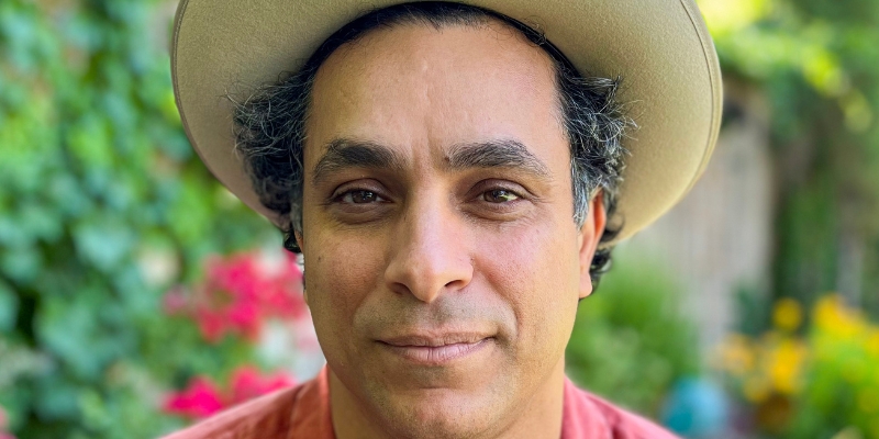 Headshot of Wesaam Al-Badry (with short black hair, tan skin, orange shirt, and beige brimmed hat)