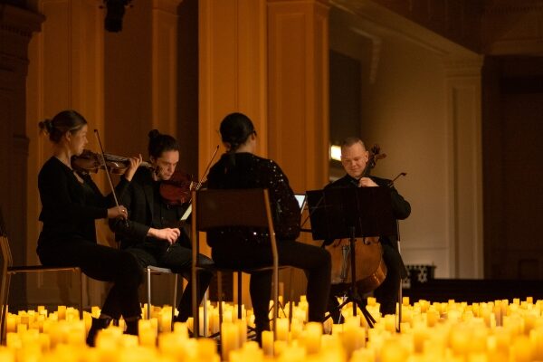 A string quartet performs on a dark stage, surrounded by lit candles.