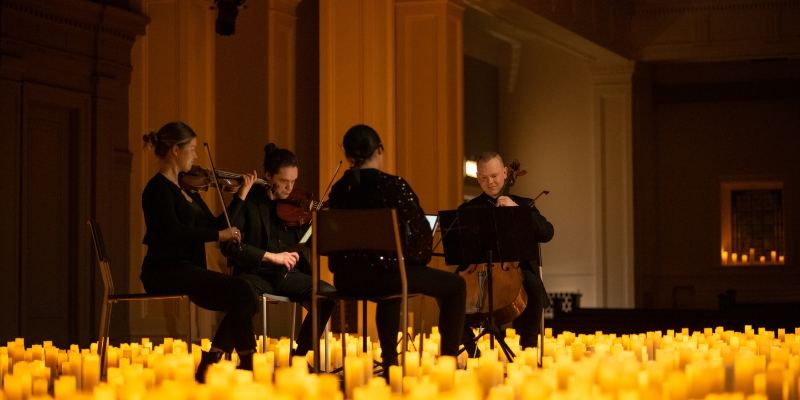 A string quartet performs on a dark stage, surrounded by lit candles.