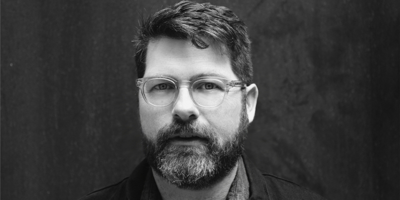 Black and white headshot of Colin Meloy (with fair skin, short hair, beard, and eyeglasses)