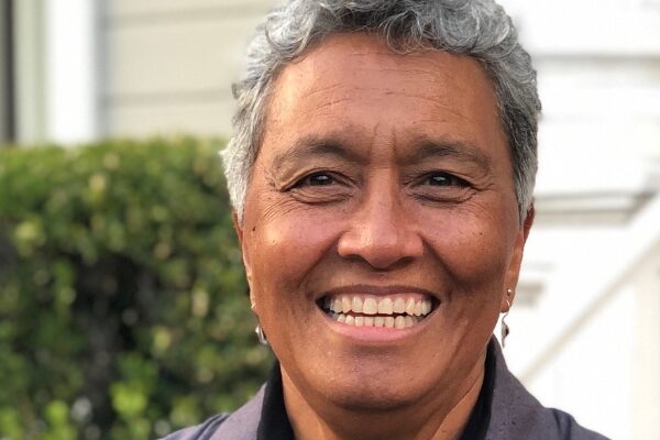 Headshot of Margo Okazawa Rey (with tan skin, short grey hair, and silver earrings)