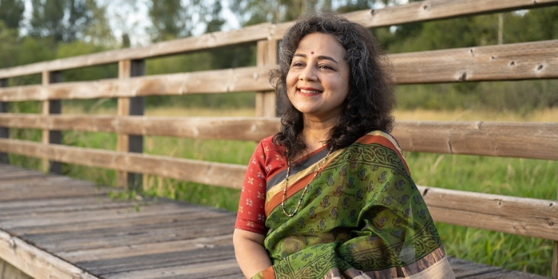 Headshot of Srivani Jade (with tan skin, shoulder length black hair, and red/green sari)