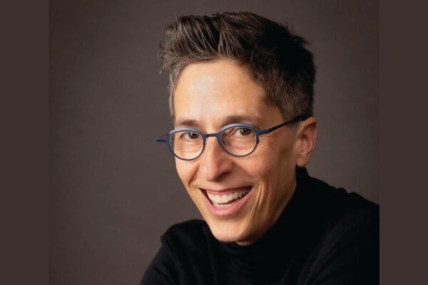 a person with glasses and a black turtleneck is smiling