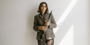 Jahnvi Madan poses and smiles holding her clarinet in front of a white wall.