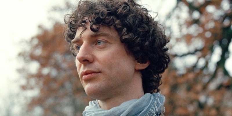 Outdoor headshot of Merlin Sheldrake (with fair skin, short curly brown hair, and blue scarf)