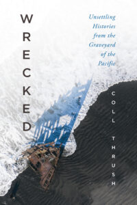 Book cover for "Wrecked" by Coll Thrush, featuring an aerial view of a shipwreck on a dark sandy beach, with foamy ocean waves washing over it. The book title "Wrecked" runs vertically on the left, with the subtitle "Unsettling Histories from the Graveyard of the Pacific" in blue text on the right.