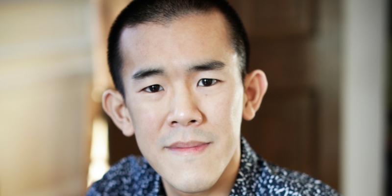 Headshot of Ed Yong (with fair skin, black buzzcut, and patterned button-down shirt)