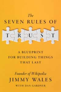 Book cover for "The Seven Rules of Trust" by Jimmy Wales, featuring a yellow background. At the top, the title "The Seven Rules of Trust" is written in elegant black serif font. Below the title, the word "TRUST" is integrated within a design of interlocking white puzzle pieces, with each letter occupying a separate piece. The subtitle "A Blueprint for Building Things That Last" is below the main title.