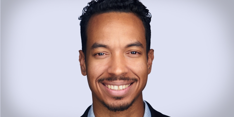 Headshot of John Wood Jr. (with tan skin, short curly black hair, and goatee)