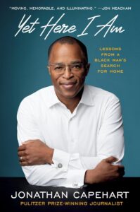 Book cover for "Yet Here I Am: Lessons From A Black Man's Search for Home" by Jonathan Capehart, featuring a photo of the author wearing a white dress shirt and smiling with his arms crossed. He poses in front of a teal background with the main book title above in white cursive text.