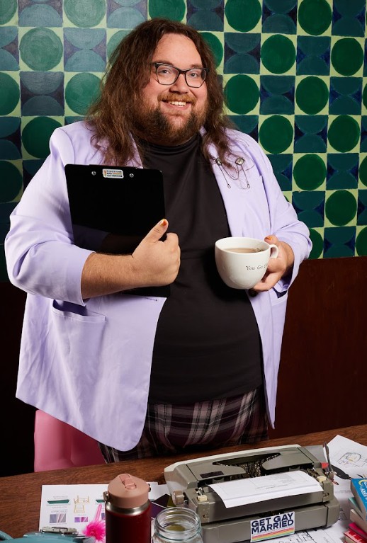 Jake Taylor in a lavender blazer holding a clipboard and coffee mug