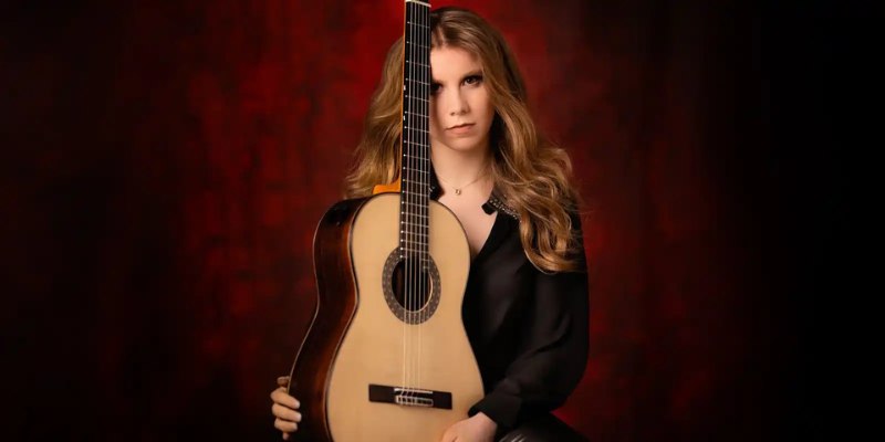 Headshot of Laura Lootens (wearing a black blouse) holding a guitar in her lap