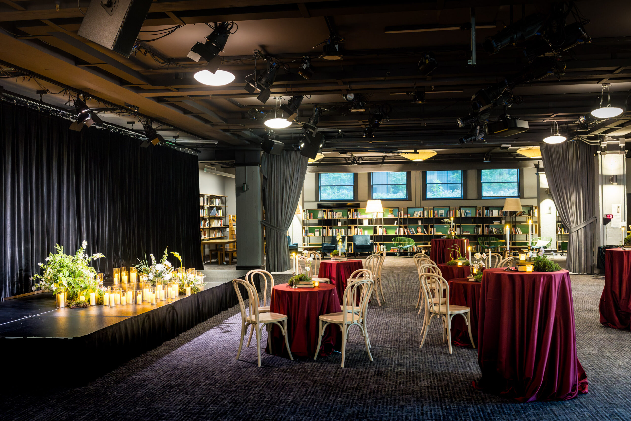 Photo of a mid-sized venue with a stage and carpeted seating area with row seating plus round tables and chairs