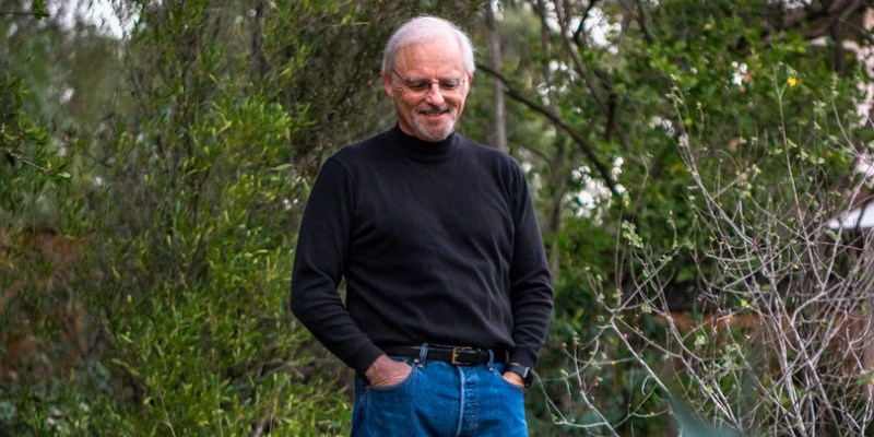 Richard Louv (with white hair, wearing a black turtleneck) smiles and stands outdoors