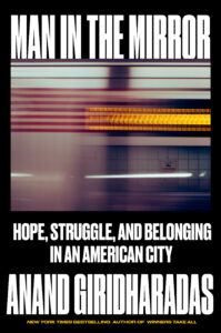 Book cover for "Man in the Mirror: Hope, Struggle, and Belonging in an American City" by Anand Giridharadas. The cover features a photo showing a subway station reflected off of the metal on a subway.