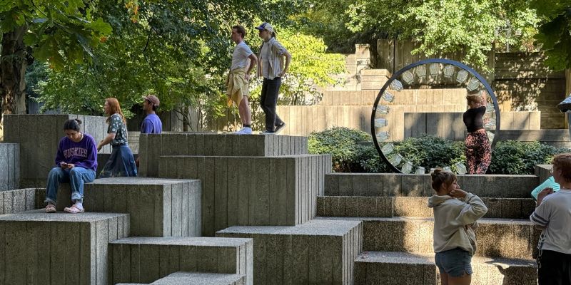 People sit and stand on various large concrete blocks outdoors.