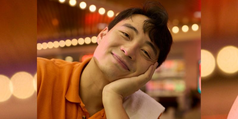 Nigel Ng (AKA Uncle Roger) in an orange shirt with face in hand.