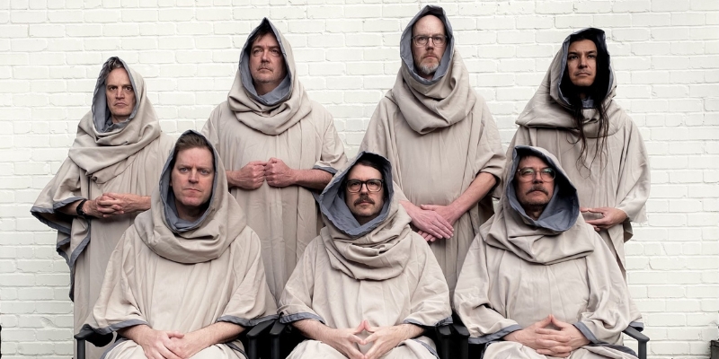 Group photo of "Awesome," featuring seven members posing while wearing hooded beige cloaks.