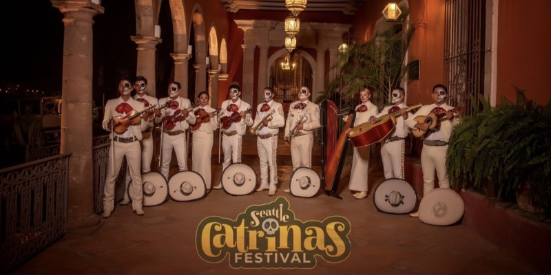 Mariachi ensemble posing and holding their violins in a warmly lit courtyard, with the “Seattle Catrinas Festival” logo at the bottom.