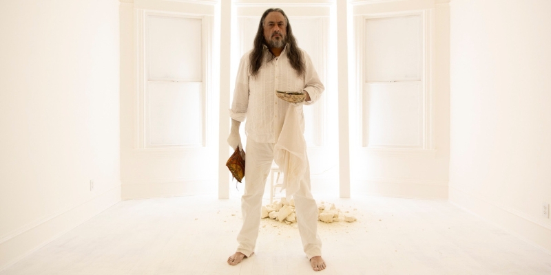 Full body photo of Timothy White Eagle, dressed in all white against a bright white background.